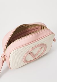 Ροζ δερμάτινη τσάντα και κρεμ υφασμάτινη τσάντα με υφή, με στρογγυλή μορφή, που διαθέτει έναν κυκλικό λογότυπο και χρυσές φερμουάρ, μερικώς ανοιχτή.