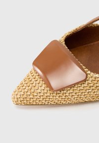 Υφασμένο κίτρινο-καφέ επίπεδο παπούτσι με μυτερή μύτη, που διαθέτει γυαλιστερή καφέ λεπτομέρεια στο επάνω μέρος και καφέ δερμάτινη σόλα.