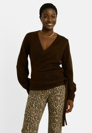 Suéter marrón con un escote en V profundo, mangas largas y un lazo lateral. Combinado con pantalones beiges con estampado de leopardo, que muestran una tela texturizada.
