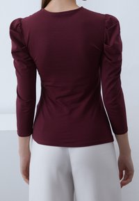 Burgundy åtsittande topp med puffärmar, rund halsringning och mjukt tyg; kombinerad med vita högmidjade byxor.