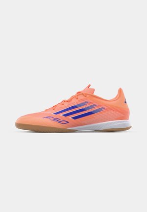 Lysorange fodboldstøvler med blå accenter, et strømlinet design, tekstureret overdel og gummisål for god greb. Model F50 vist fra siden.