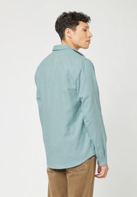 Lichtblauw geruit overhemd met lange mouwen en een puntige kraag, gecombineerd met beige corduroypantalon.