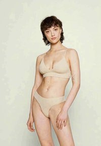 Beige színű fehérnemű szett, puha anyagból; állítható pántos bralette-t és hozzá illő magas derekú tanga bugyit tartalmaz, varrás nélküli dizájnnal.