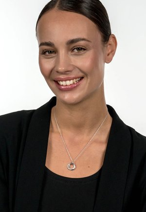 Silberne Halskette mit einem runden Anhänger mit strukturierten Oberfläche, aufgehängt an einer zarten Kette, getragen über einem schwarzen Oberteil.
