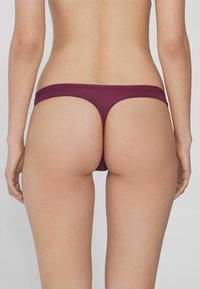 String bordeaux avec un design sans couture, une taille élastique et une couverture arrière minimale, fabriqué à partir d'un tissu doux et extensible.