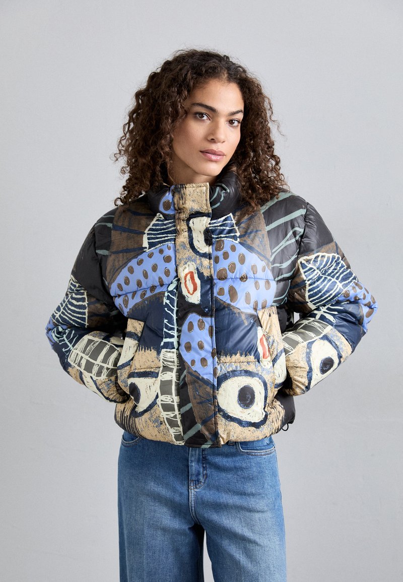 Giacca imbottita con motivi astratti colorati in blu, nero e crema. Caratterizzata da un colletto alto e una chiusura con zip. Finitura morbida e texturizzata.