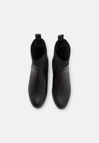 Černé kožené kotníkové boty s hladkým povrchem, elastickými bočními panely a poutky pro snadné nazouvání. Mají štíhlý, minimalistický design.