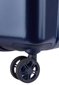 Maleta dura color azul marino con una textura suave, que cuenta con una rueda negra de múltiples radios y un alojamiento de rueda reforzado para mayor durabilidad.