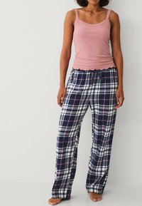 Lichtroze tanktop met kantafwerking, gecombineerd met marineblauwe geruite pyjamabroek met witte en roze accenten, relaxte pasvorm en een verstelbare tailleband.