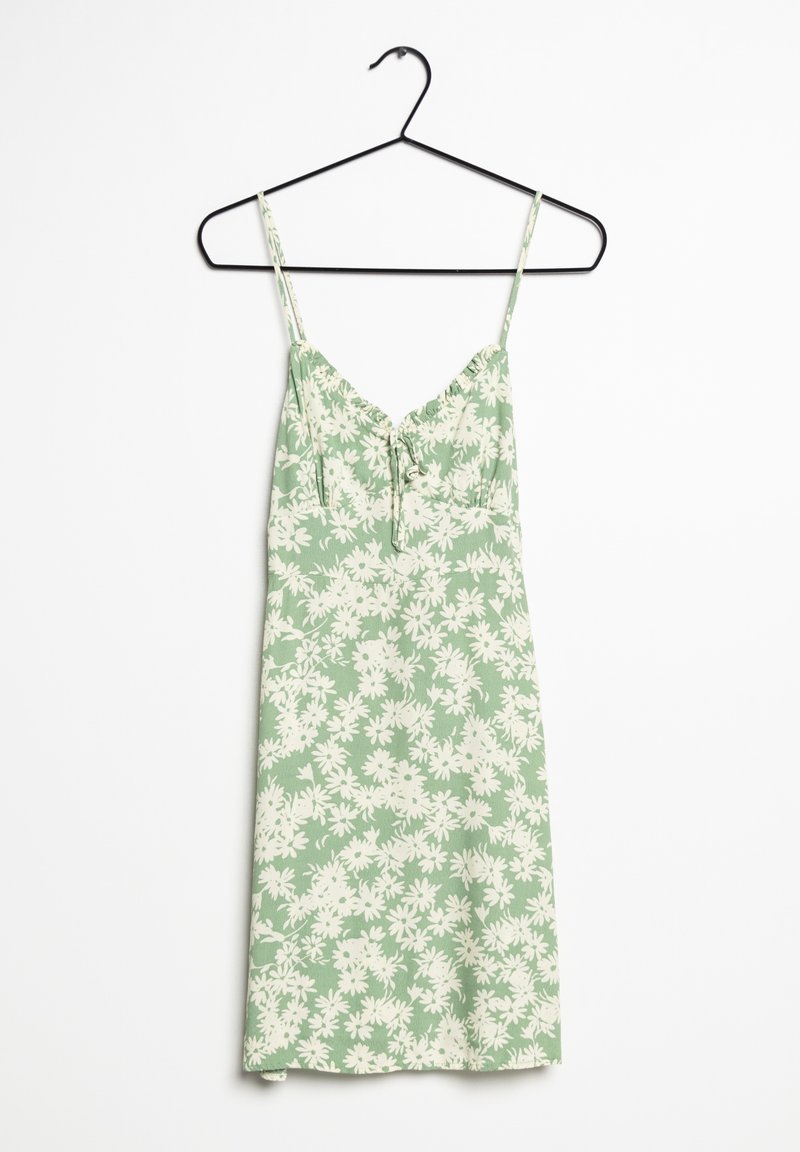 Robe sans manches vert clair avec imprimé floral blanc et fines bretelles suspendue sur un cintre noir sur fond blanc.