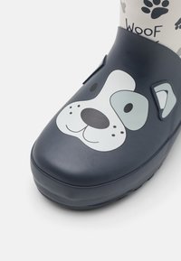 Botte en caoutchouc bleu marine avec un design de visage de chien sur le bout, présentant des accents blancs, gris et noirs, et des motifs de pattes sur la tige.