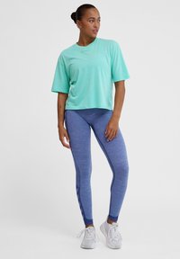 Lys mintgrøn kortærmet atletisk skjorte parret med blå teksturerede leggings. Hvide sneakers fuldender outfittet. Enkel, sporty design.