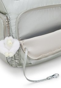 Borsa in nylon morbido di colore argento con una texture liscia e una tasca con zip. Presenta un portachiavi a forma di orsetto soffice e un'attacco a clip argentato.