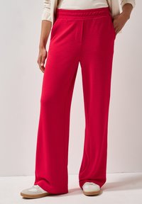 Rode, ontspannen pasvorm wijde broek met een getextureerd ribbelpatroon, elastische tailleband en zijzakken. Gedragen met lichtgekleurde schoenen.