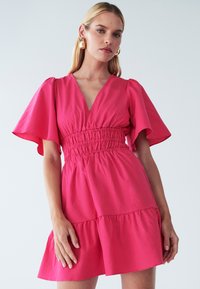 Rosa Baumwollkleid mit V-Ausschnitt, kurzen, ausgestellten Ärmeln und gerafftem Taillenbereich. Verfügt über einen gestuften Rock und eine glatte Textur.