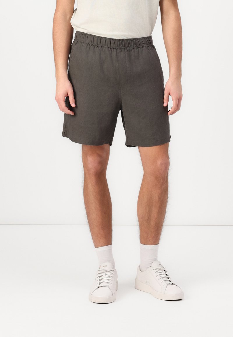 Shorts en lin gris foncé avec une taille élastique, des poches latérales et une coupe décontractée, associés à des baskets blanches et des chaussettes mi-mollet.