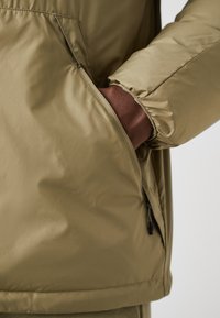 Alyvų spalvos pūkinė striukė su užtrauktuko šoniniu kišeniu, elastingomis rankogaliais ir lygiu, matinio tekstūros paviršiumi.
