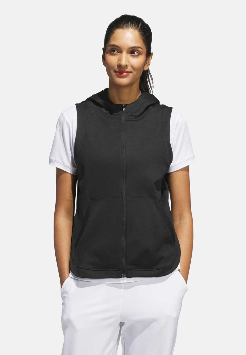 Black sleeveless hooded vest with a front zipper and two pockets, worn over a white short-sleeve shirt. Smooth fabric texture.