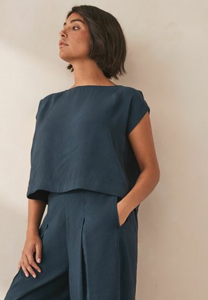 Marinblå kort topp med avslappnad halsringning och korta ärmar, tillverkad av ett texturerat tyg, i kombination med matchande löst sittande byxor.