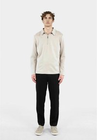 Ljusbeige zip-up tröja med krage, långa ärmar och en jämn textur, kombinerad med svarta byxor och ljusgrå sneakers.