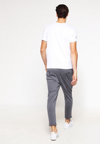 Camiseta blanca de manga corta combinada con pantalones entallados gris con rayas finas y zapatillas blancas, mostrando un ajuste casual y relajado desde atrás.