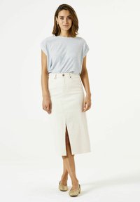 Camiseta a rayas azul claro con mangas enrolladas, combinada con una falda midi de mezclilla blanca con una abertura frontal y cierre de botones. Lleva zapatos beige sin talón.