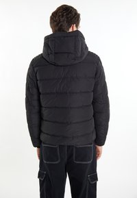 Jachetă neagră matlasată cu glugă, având panouri orizontale matlasate și o textură netedă. Purtați cu pantaloni cargo negri.