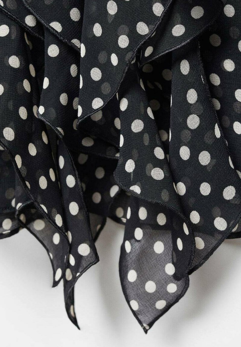Schwarzer transparenter Stoff mit weißen Punkten, versehen mit geschichteten Rüschen mit einem rohen Saumfinish. Weiche Textur und leichtes Design.