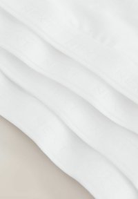 Stablet af foldet hvid bomuldsstof med subtilt præget branding eller tekst synlig på overfladen.