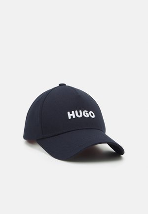 Casquette de baseball bleu marine avec une visière courbée, ornée du texte "HUGO" brodé en blanc sur le panneau avant, présentée sur un fond blanc.