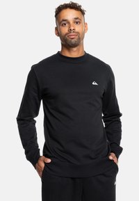 Czarny sweter z miękkiego materiału, z okrągłym dekoltem, ściągaczami przy rękawach oraz małym białym logo na piersi. Prosty i klasyczny design.