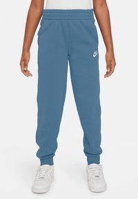 Mėlynos sportinės kelnės su raišteliu juosmenyje, elastingomis rankovėmis ir šoninėmis kišenėmis. Kairiajame šlaunyje yra baltas Nike logotipas.