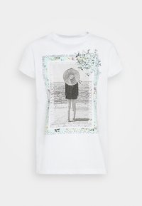 Camiseta blanca de manga corta con un estampado gráfico de una figura con sombrero junto al mar, adornada con acentos florales y texto.