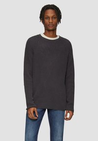 Dunkelgrauer gestrickter Pullover mit langenÄrmeln, rundem Ausschnitt und geripptem Muster, über einem hellbeigen Hemd getragen. Die Passform ist locker.