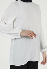 Weiße Bluse mit langen Ärmeln aus leichtem Stoff und lässiger Passform. Verfügt über geraffte Manschetten und einen runden Ausschnitt. Glatte Textur.