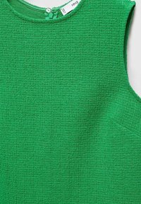 Haut sans manches vert en tissu texturé, avec un col rond et une petite poche sur le côté gauche. Fermeture par bouton au dos.