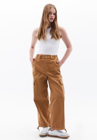 Beige cargobroek met een losse pasvorm, elastische taille, zijzakken en gathered hemden. Gecombineerd met een aansluitend wit tanktop en witte sneakers.