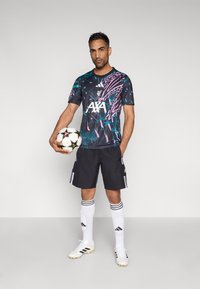 Sort og farverigt mønstret fodboldtrøje med "AXA"-logo, sorte shorts, hvide strømper og hvide fodboldstøvler, der holder en fodbold.