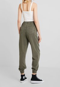 Olivgröna joggerbyxor med elastiska muddar och bakfickor, kombinerat med svarta högskoor och en vit ribbad tanktop.