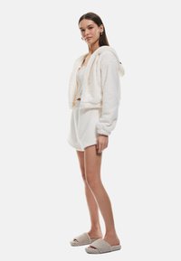 Conjunto de chaqueta con capucha y pantalones cortos en suave tela blanca; forro de felpa texturizado con un ajuste relajado y mangas oversize. Zapatillas color crema.