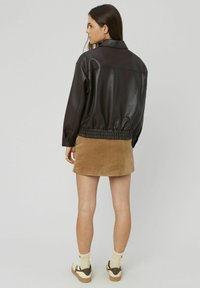 Veste en simulateur de cuir marron avec ceinture élastique, à associer avec une jupe en velours côtelé beige. Des baskets blanches et marron avec des chaussettes jaunes complètent le look.