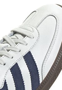 Vita lädersneakers med marinblå mockastripes, texturerad gummisula och grå sömmar. Snören är gjorda av ljusgrått tyg.