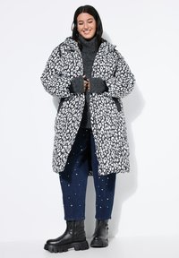 Chaqueta de plumas de estampado de leopardo en blanco y negro con capucha, puños de punto acanalado y bolsillos laterales, combinada con jeans oscuros con acentos de perlas.