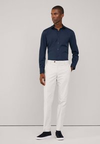 Camisa de botones azul marino de manga larga, combinada con pantalones ajustados blancos y zapatillas oscuras. Tejido suave con un diseño entallado.
