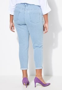 Světle modré skinny džíny s ohrnutými lemy, dvěma zadními kapsami a detailem vázání v pase, doplněné fialovými semišovými lodičkami na vysokém podpatku.