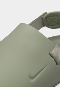 Ανοιχτό πράσινο σανδάλι Nike slip-on με πίσω λουράκι και υφή στη σόλα, που δείχνει το ανάγλυφο λογότυπο στην λεία επάνω επιφάνεια.