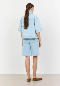 Svjetloplava traper jakna sa širokim krojem i širokim rukavima u kombinaciji s kratkim hlačama do koljena, koje imaju stražnje džepove i šavove.