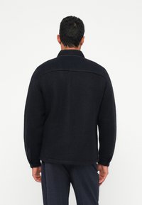 Zwarte fleecejas met een gestructureerde kraag, textuurstof en lange mouwen, voorzien van een achterpand en details aan de zijnaden.