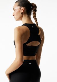 Sort atletisk crop top med racerback skæring og en åbning på ryggen. Parret med højhalset sorte leggings.