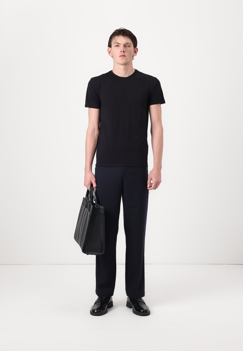 Juodas medvilninis marškinėlis, tamsiai mėlyni pritaikyti kelnių, juoda odinė kuprinė su keliais skyreliais ir juodi batai. Paprastas, struktūruotas dizainas.